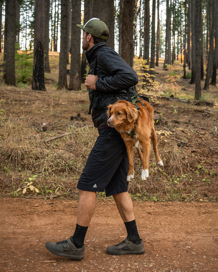 Man carrying his Toller on MTB trail with the K911 Rescue Sling paired with the Lander harness in Trail Green color