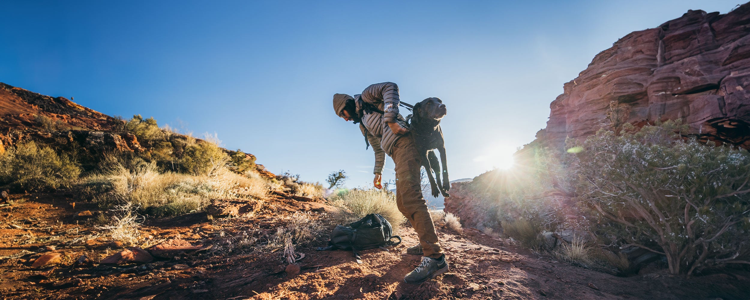 man lifting his injured black dog in the desert with the k-911 rescue sling