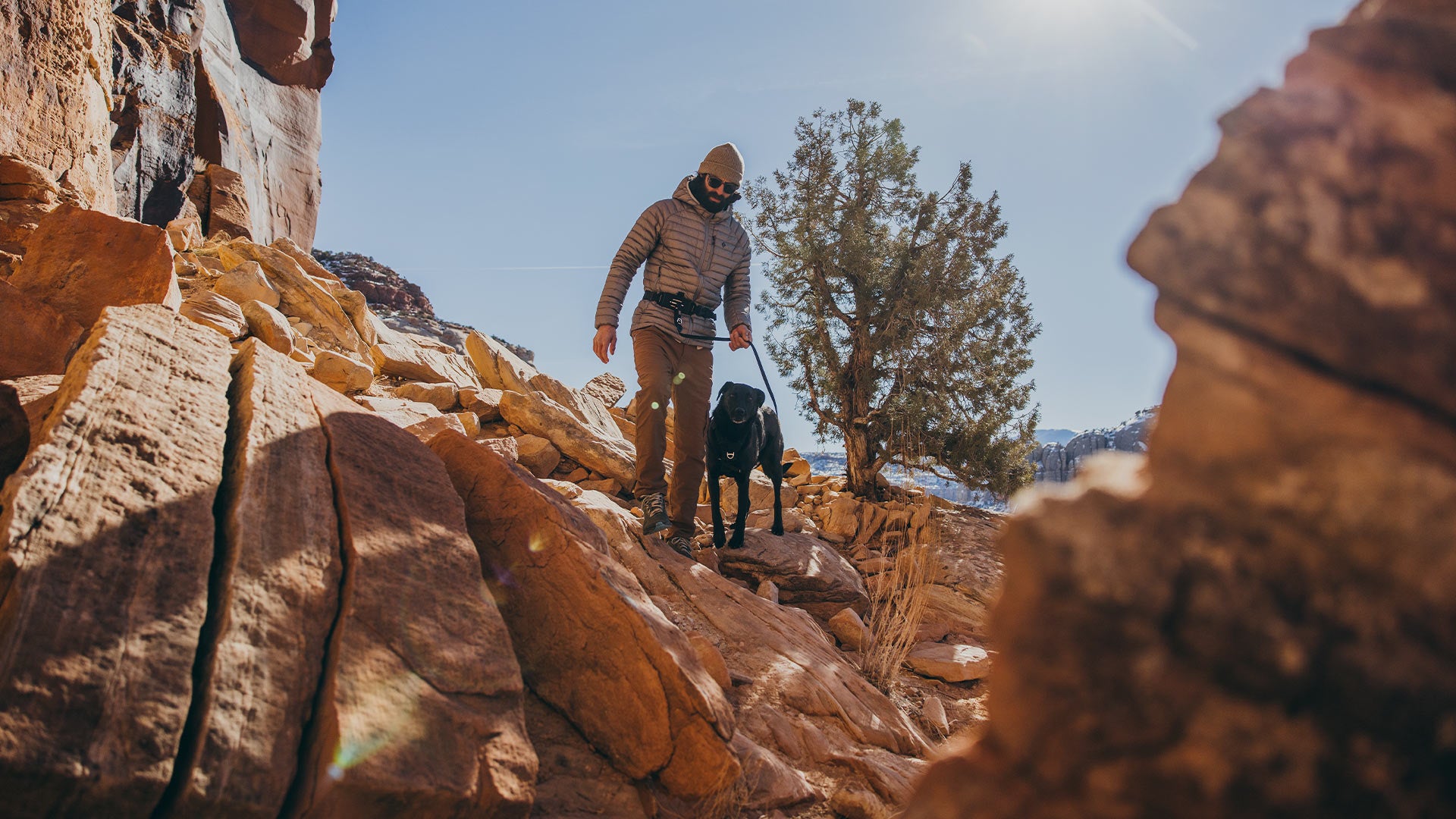 man walking through rocks with his black dog wearing the canyon light core