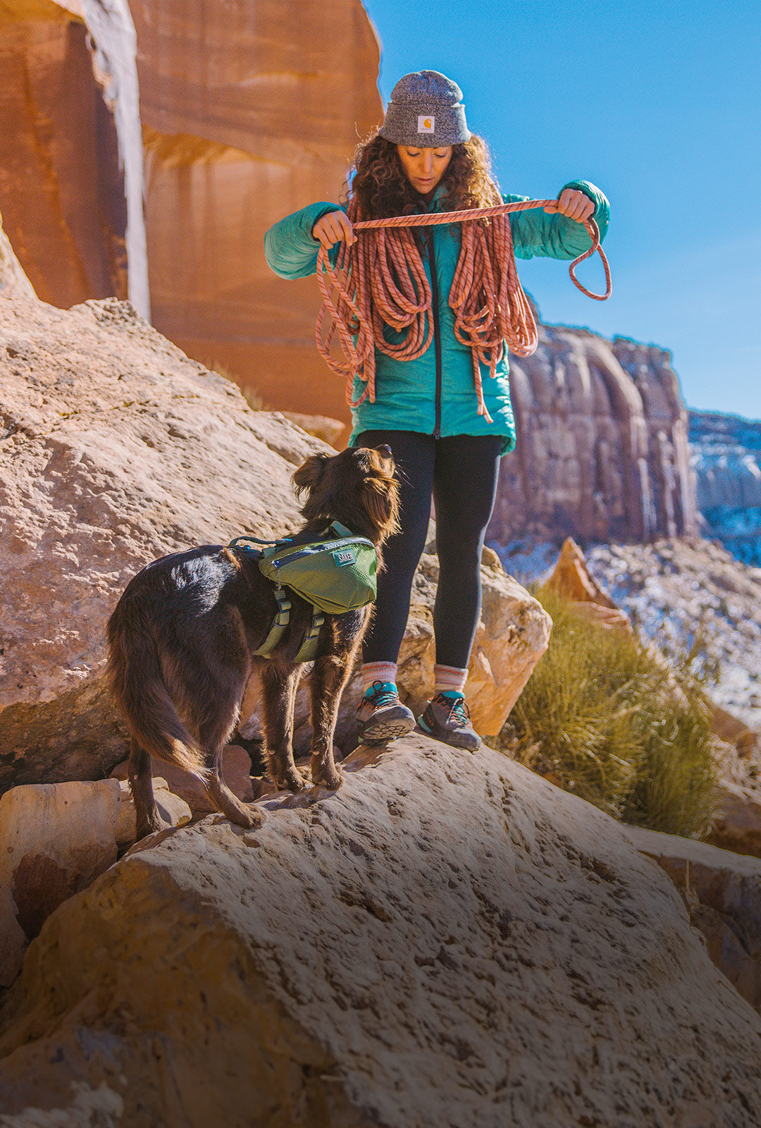 Woman wrapping rope around her back with her dog wearing the canyon pro pack in moss green