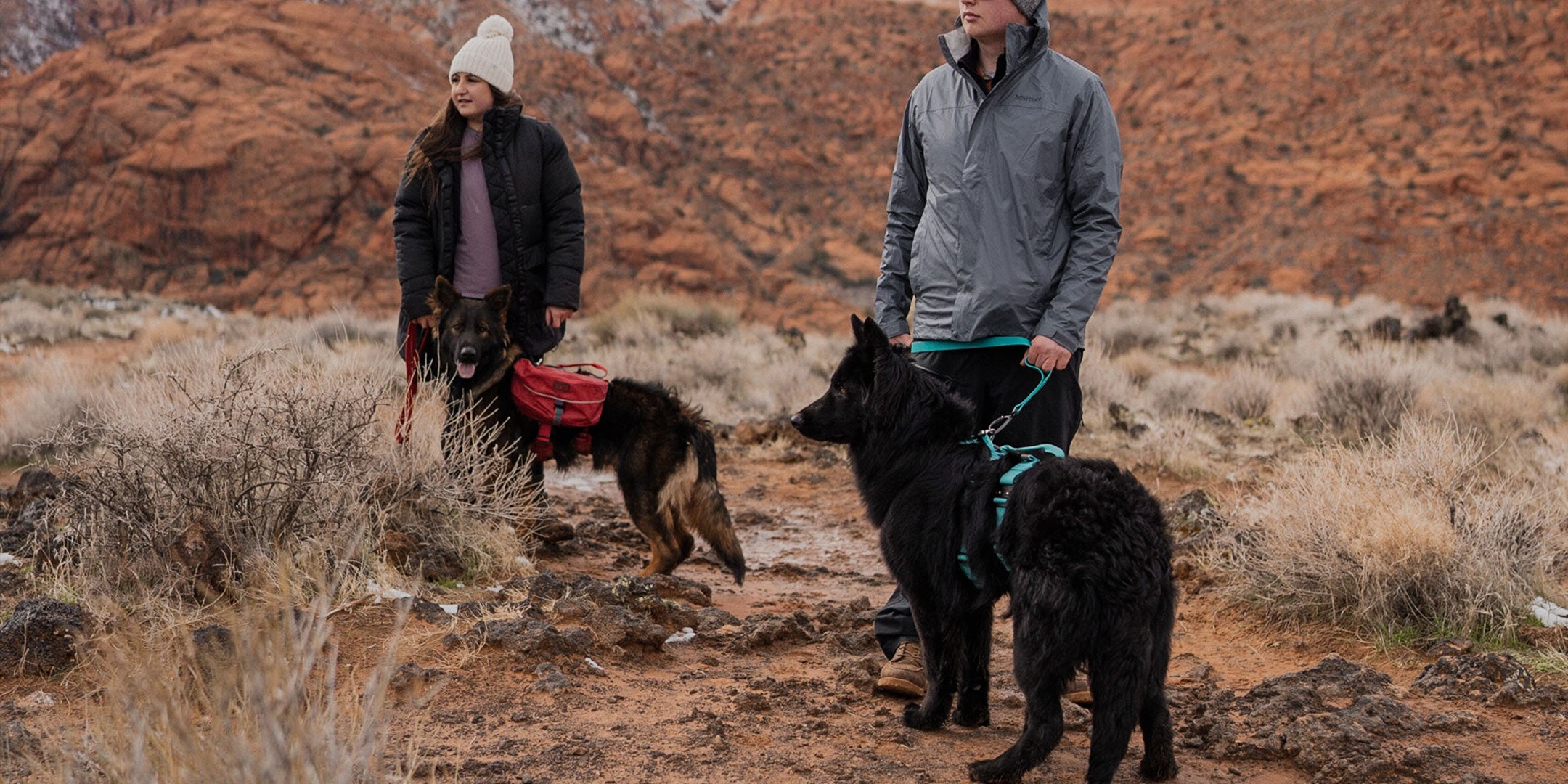 couple exploring lava caves with their two gsd each wearing the saker harness. one has the blazing red dog pack, the other has the tazer teal extended harness