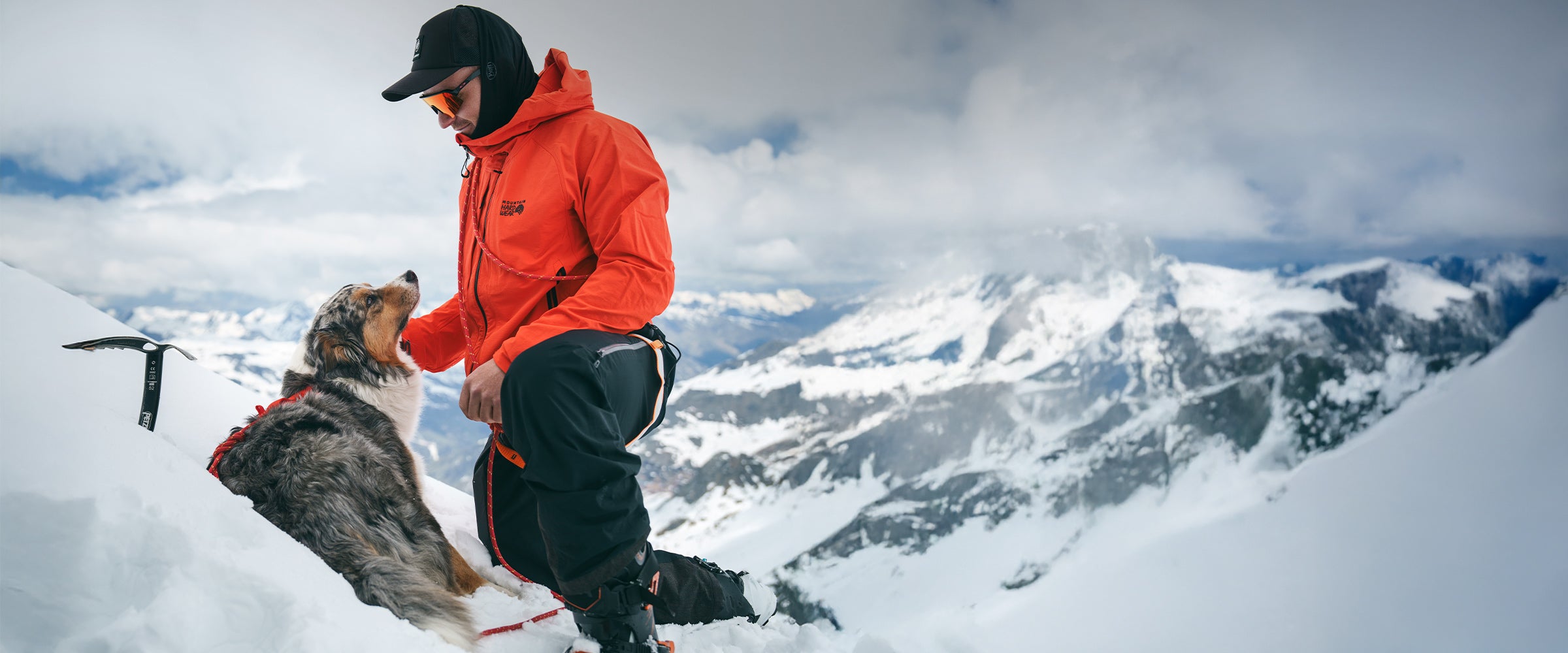 Mountaineer with his dog in the Alps. His dog is wearing the Lander harness in Alpine Orange