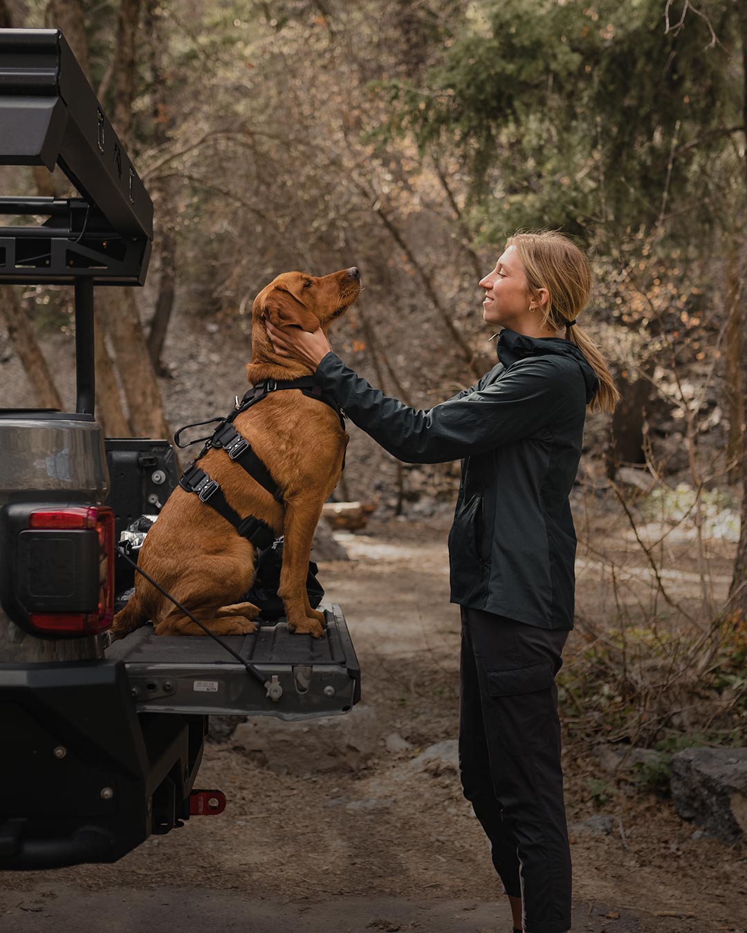 Woman petting her dog  wearing the extended Ascension in the trunk of jeep