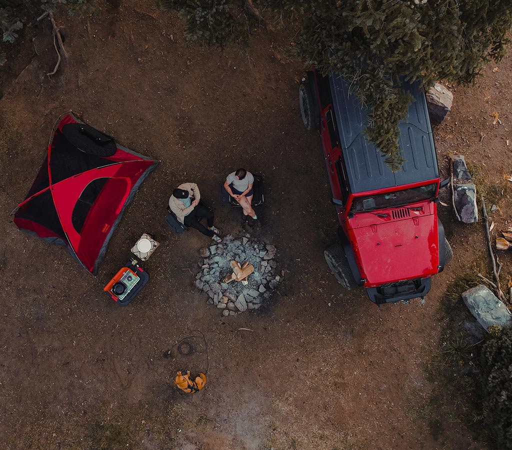 Drone top view of a couple and dog at campsite. The dog wears the ascension extended harness and is tied to the gravity dog tie out stake