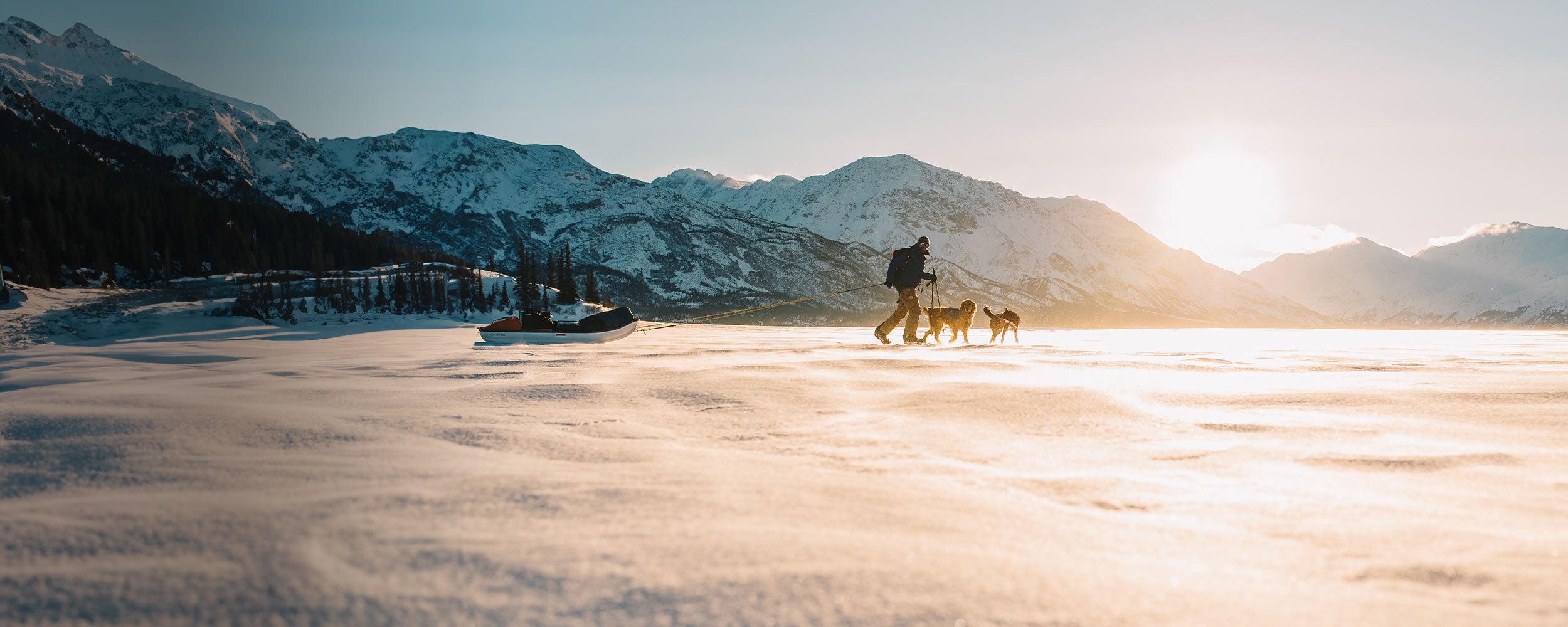 Man pulling sled on a frozen lake in Yukon with his two dogs wearing the Canyon Light Pack
