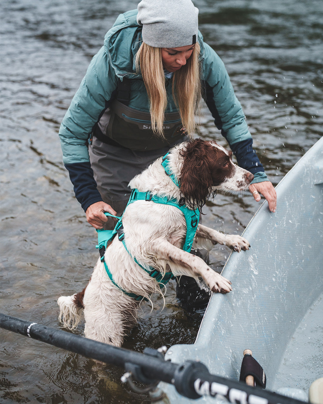 Paula Shearer lifting her dog Willow into her boat. Her dog is wearing the Saker Muse harness in Skeena Teal