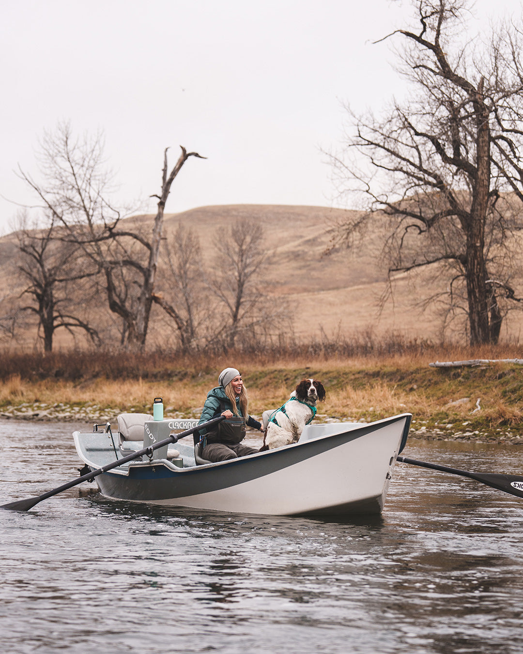 Paula Shearer in her boat with her dog Willow on the Bow River. Her dog is wearing the Saker Muse harness in Skeena Teal