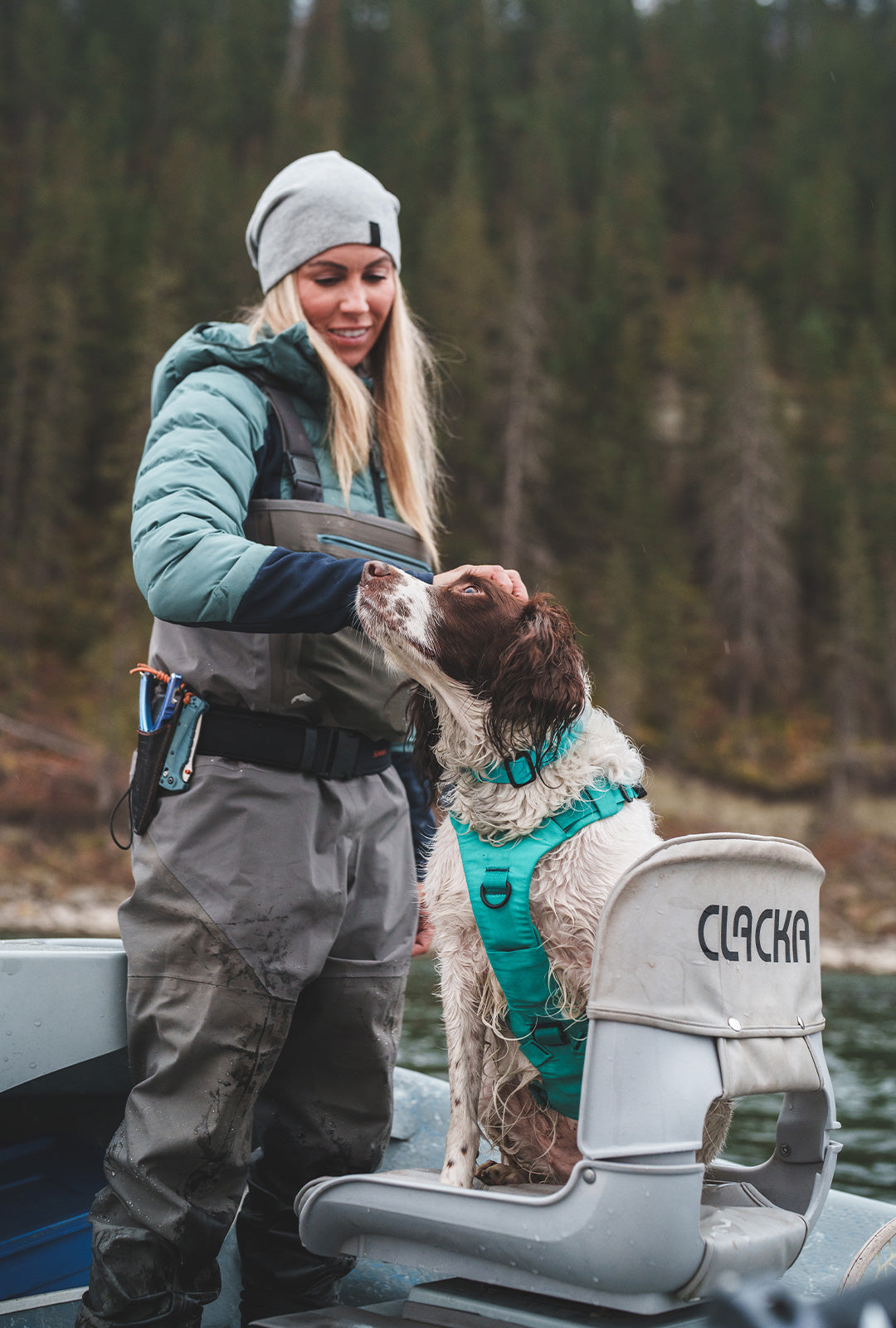 Woman petting her fishing dog that wears a Skeena Teal Muse harness in her fishing boat