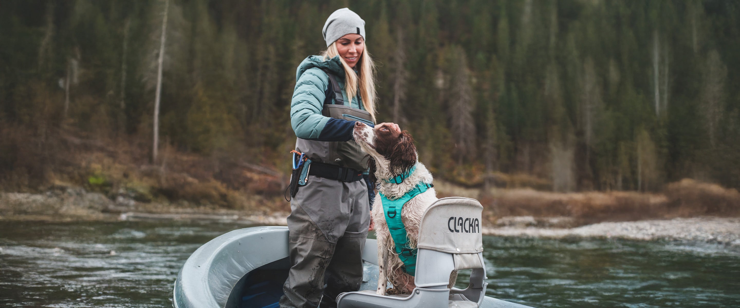 Woman petting her fishing dog that wears a Skeena Teal Muse harness in her fishing boat